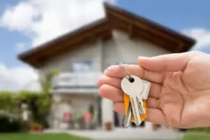 hand-holding-keys-in-front-of-california-two-story-house-with-balcony